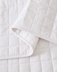 A close-up of a white quilted bedding item, likely a duvet cover or sheet, folded over to show its stitched grid pattern and clean fabric texture.