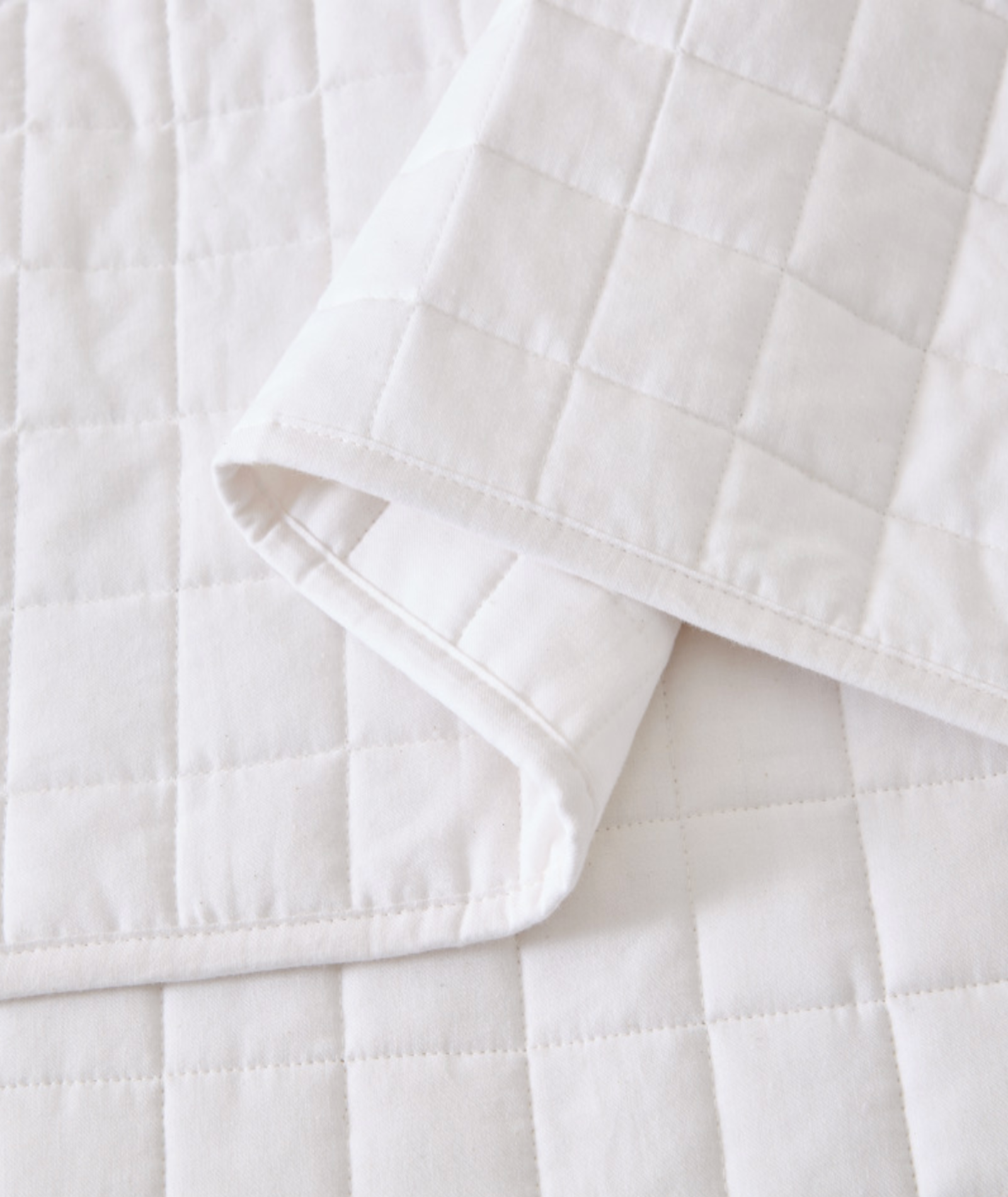 A close-up of a white quilted bedding item, likely a duvet cover or sheet, folded over to show its stitched grid pattern and clean fabric texture.